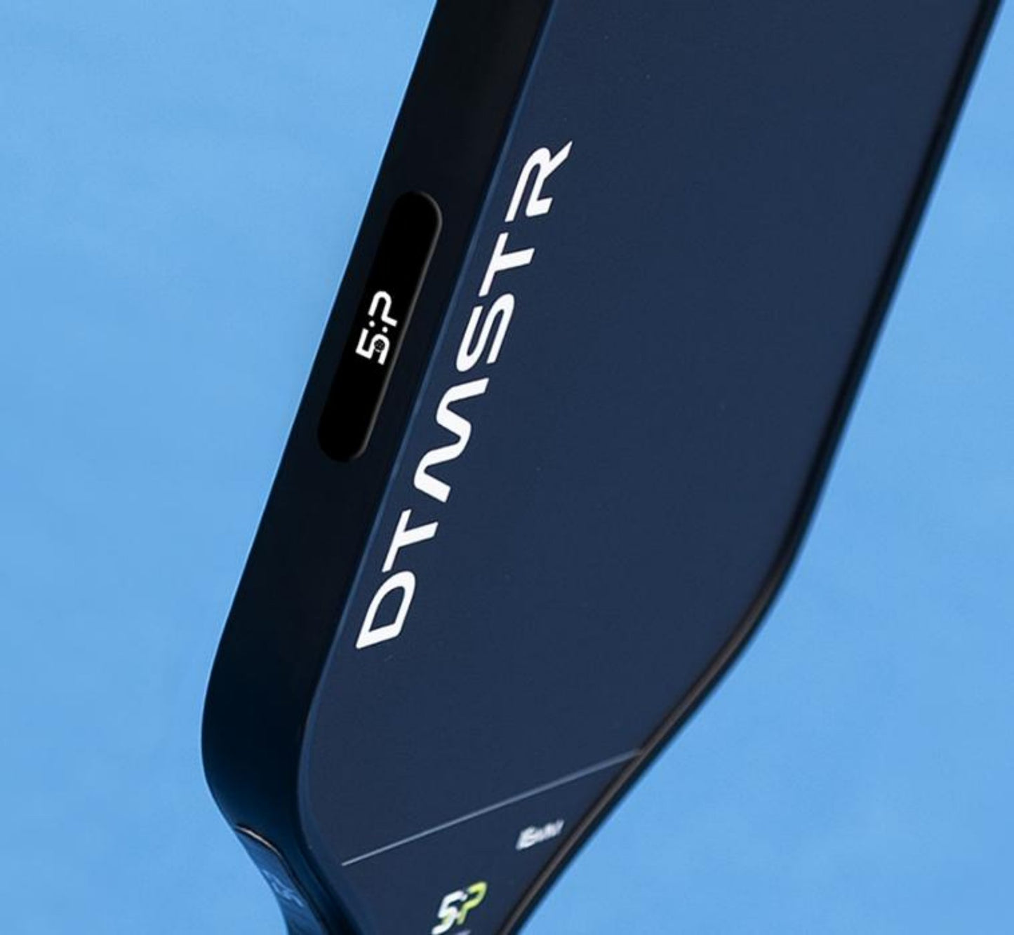 A close-up image of a Picklepacks pickleball paddle by 5 O'clock Pickleball displays the text DTMSTR on the edge. The dark surface of the paddle includes a small label, "5:5," near the handle, suggesting expert customization. The backdrop is a light blue color.