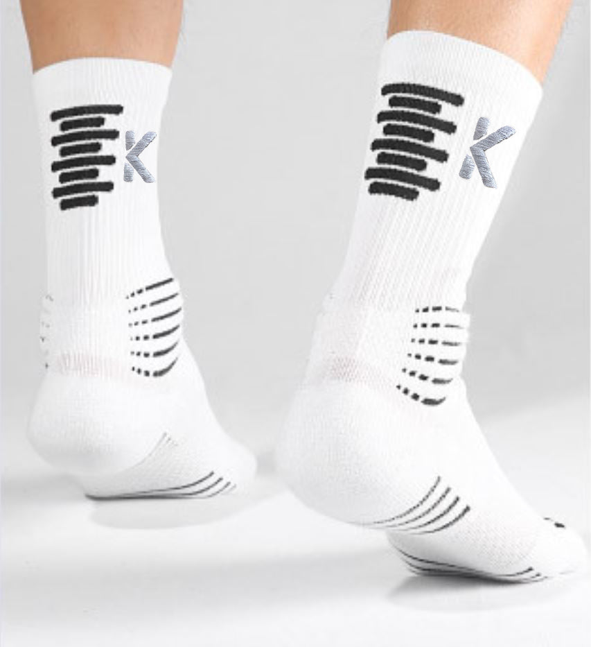 A person stands on a white surface, wearing Klyng's PowerStep Achilles Support Compression Socks, which are white with black stripes and feature a gray K design on the back.