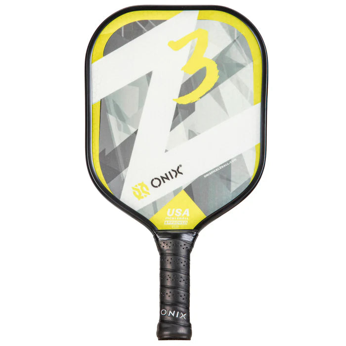 A close-up of the Onix Z3 Pickleball Paddle highlights its geometric design in gray, white, and yellow. The number 3 is prominently displayed on its composite surface. This paddle features a wide body shape and a black handle with the Onix logo at the base.