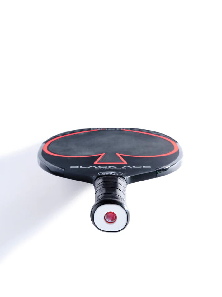 A black and red pickleball paddle lies face up against a white background, showcasing its handle wrapped in black grip material. This TORAY faced carbon paddle by Prokennex is equipped with cutting-edge kinetic technology for enhanced performance.