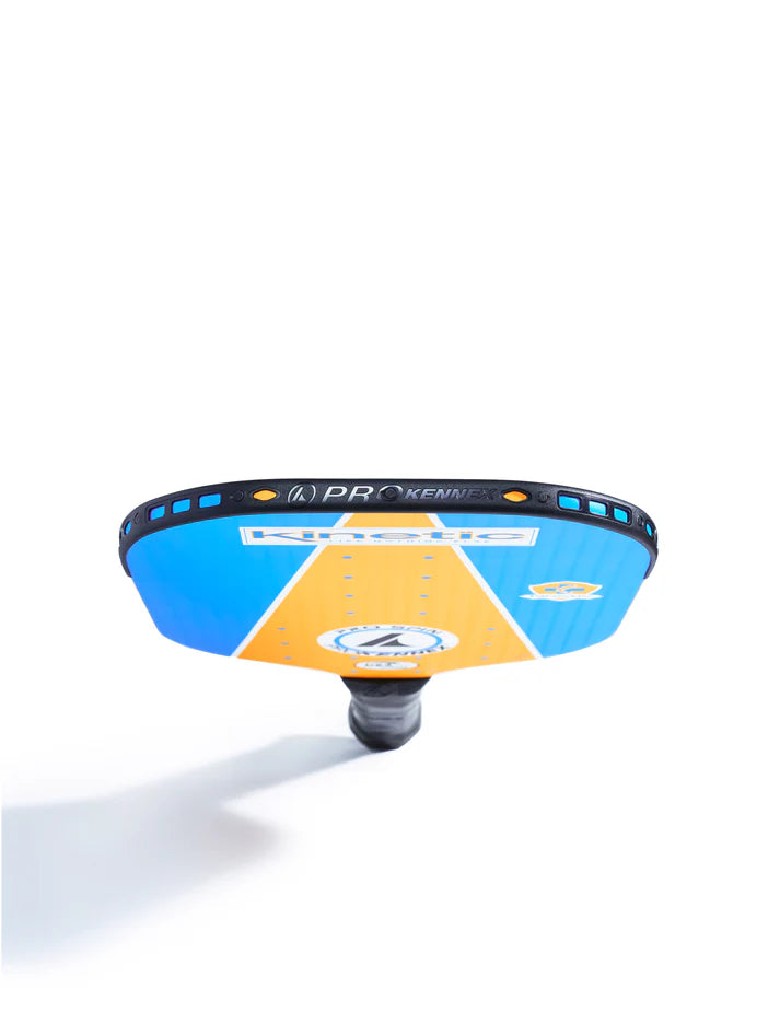 Introducing the Prokennex Pro Spin Pickleball Paddle, a striking blue and orange design featuring a unique geometric pattern. Engineered with Pro Spin technology for superb spin control, this paddle is depicted standing vertically with its handle at the bottom and casting a shadow.