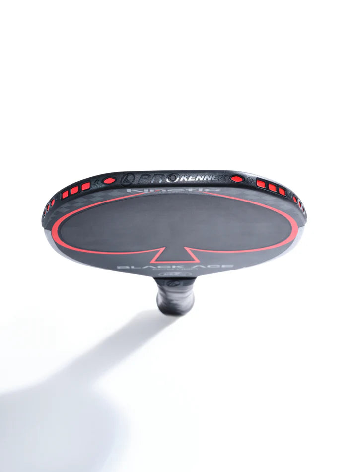 Close-up of a Prokennex Black Ace Ovation pickleball paddle featuring TORAY faced carbon. The paddle showcases a striking black and red design on the surface, positioned vertically against a white background. The handle is visible, highlighting kinetic technology branding around its edge.