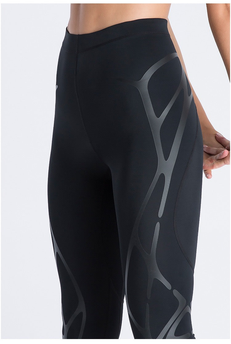 Close-up of a person wearing the Klyng Women’s PowerFlex Pickleball Compression Pants, featuring sleek black athletic leggings with abstract dark gray patterns on the sides. The design is modern and perfect for muscle support during activity. The person is posing with their hands resting on their hips, highlighting these stylish pickleball compression pants.