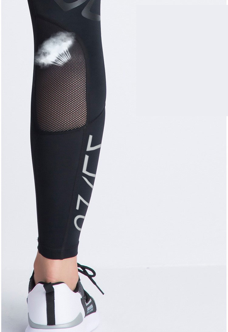 A person is wearing Klyng's Women’s PowerFlex Pickleball Compression Pants in black, featuring a mesh panel and print design with the word LYNX vertically. These leggings provide muscle support and pair stylishly with white and black athletic sneakers.