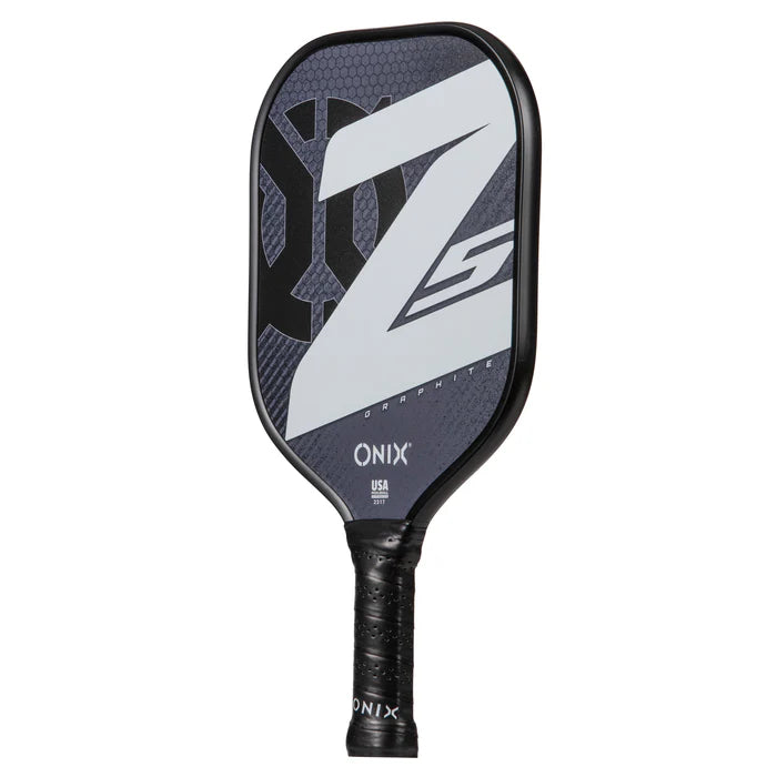 The Onix Graphite Z5 v3 pickleball paddle, available in black, showcases a distinctive white design on its face. Featuring a textured handle for a secure grip and displaying "Graphite" and "USA" prominently near the top, this pickleball paddle is an excellent choice for enthusiasts.